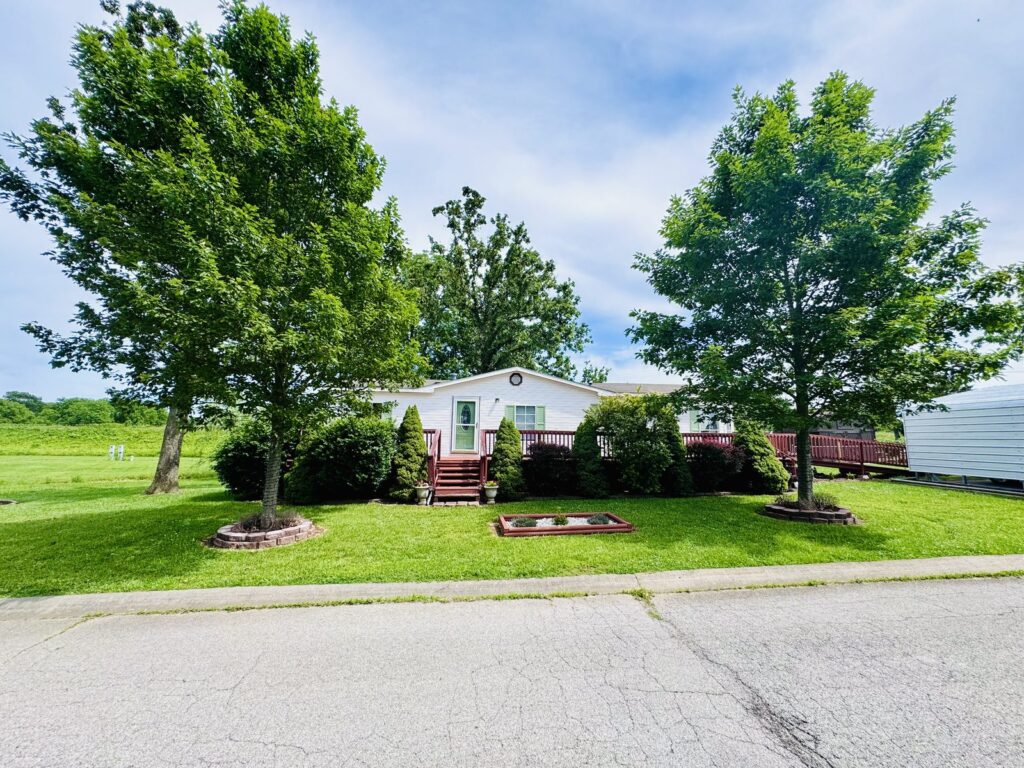 Manufactured home framed by mature trees at Cedar Glen Mobile Home Park, Aurora, MO